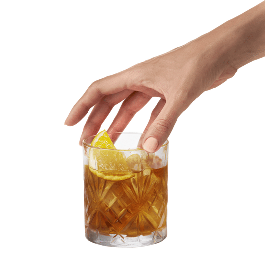 Un verre decoratif avec un cocktail et bout du citron, la main touche le verre